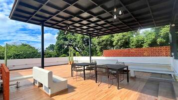 Une terrasse extérieure avec un plancher en bois, un banc blanc et une table avec des chaises.