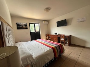 Un dormitorio con una cama, un escritorio, una silla, un televisor y una ventana.