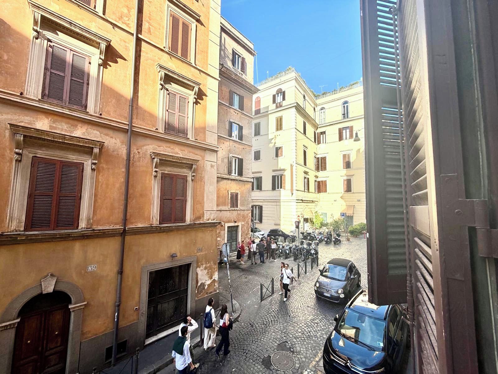 A cobblestone street with historic buildings, a group of people, and parked cars.
