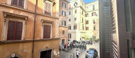 A cobblestone street with historic buildings, a group of people, and parked cars.