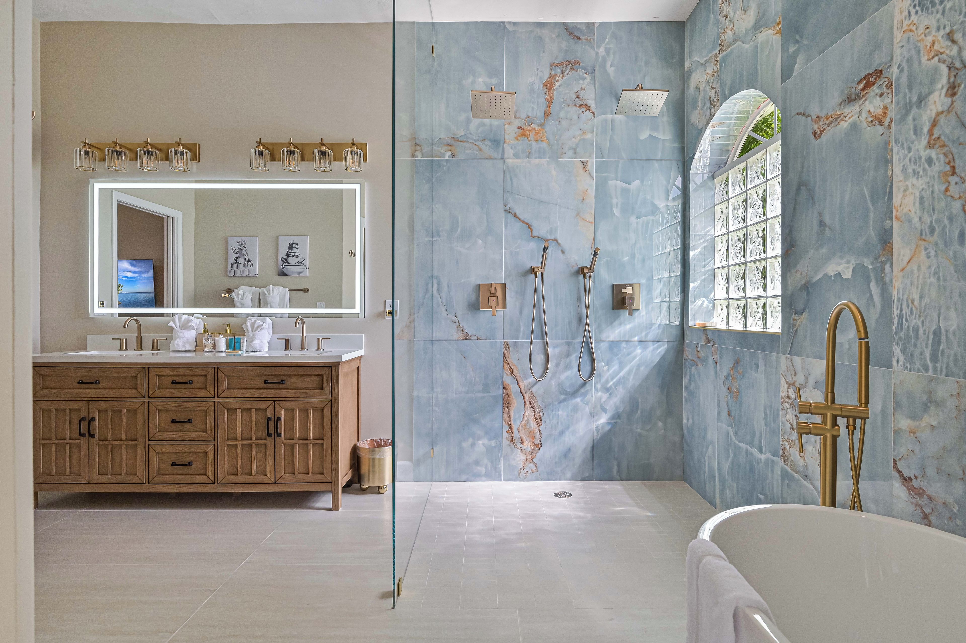 Une salle de bain avec un mur en marbre, un grand miroir, une baignoire et un meuble-lavabo avec un évier.