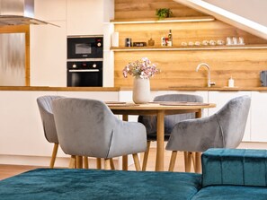 A modern kitchen with a dining area featuring a wooden table and grey upholstered chairs. - Loft Park Olomouc - Spacious 109 m² Loft with AC in City Centre (Olomouc)