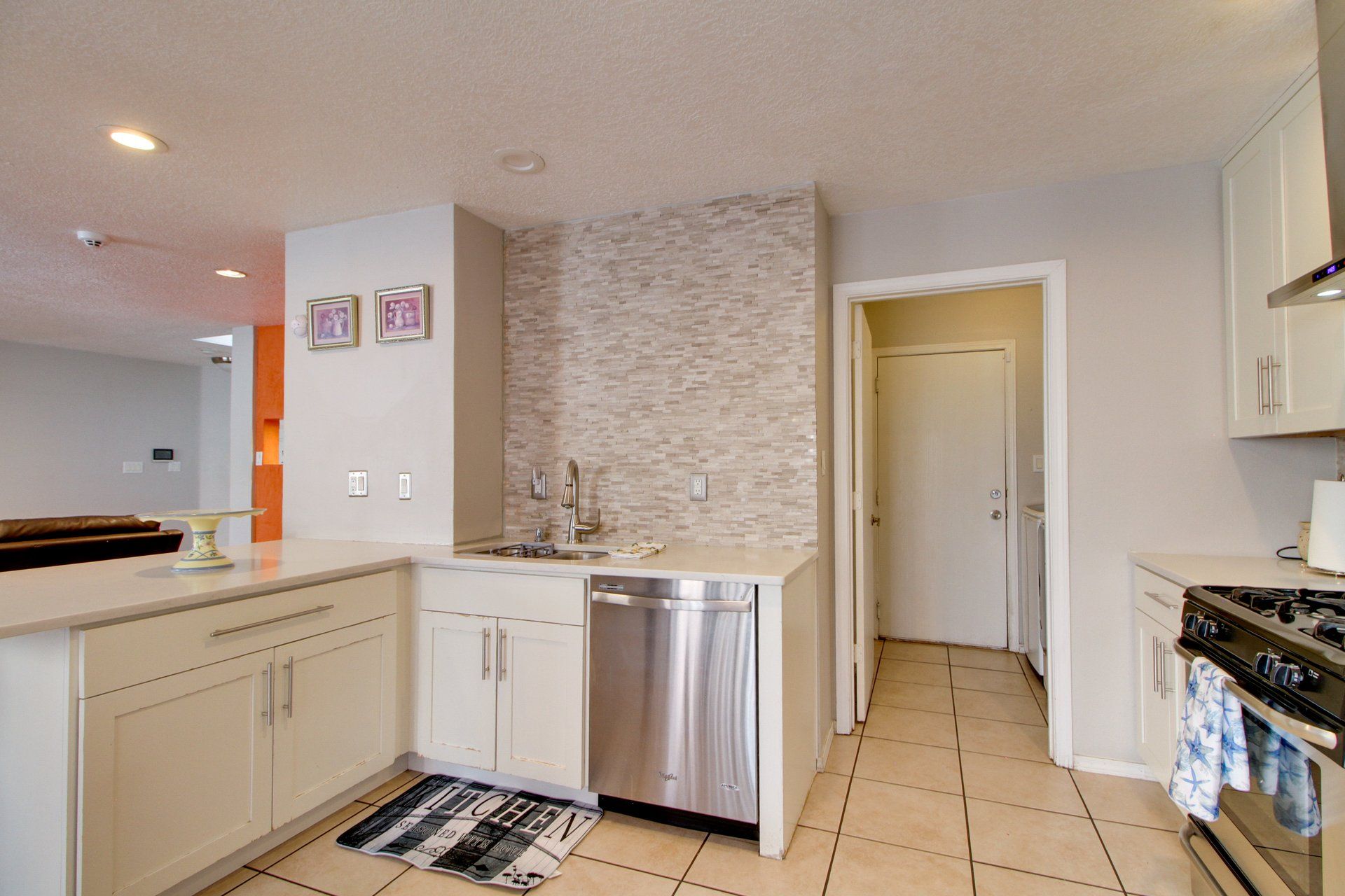 A kitchen with white cabinets, a stainless steel dishwasher, a tiled backsplash, and a stove.