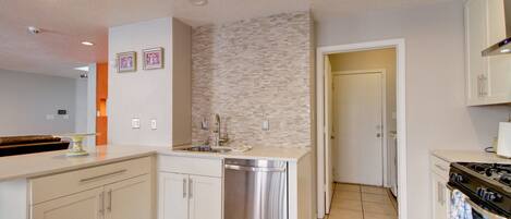 A kitchen with white cabinets, a stainless steel dishwasher, a tiled backsplash, and a stove.