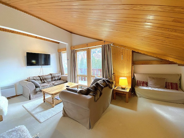 A cozy living room with a wooden ceiling, a flat-screen TV mounted on the wall, a sofa, a coffee table, and a lamp. - Apartment in Méribel, mountain view - 5 guests (Méribel)