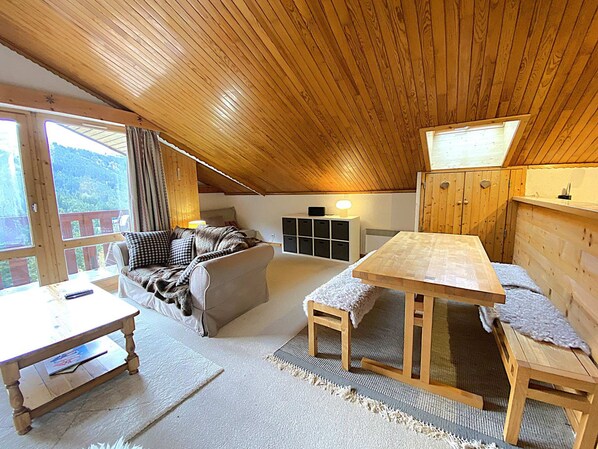 Acogedor cuarto ático con techo de madera, un sofá, una mesa y vista al exterior.