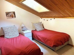 Un dormitorio con dos camas individuales, una mesita de noche, una lámpara, un cuadro en la pared y un tragaluz.