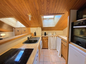 Una cocina compacta con muebles de madera, un lavamanos negro, un lavavajillas Bosch y una ventana sobre el lavamanos.