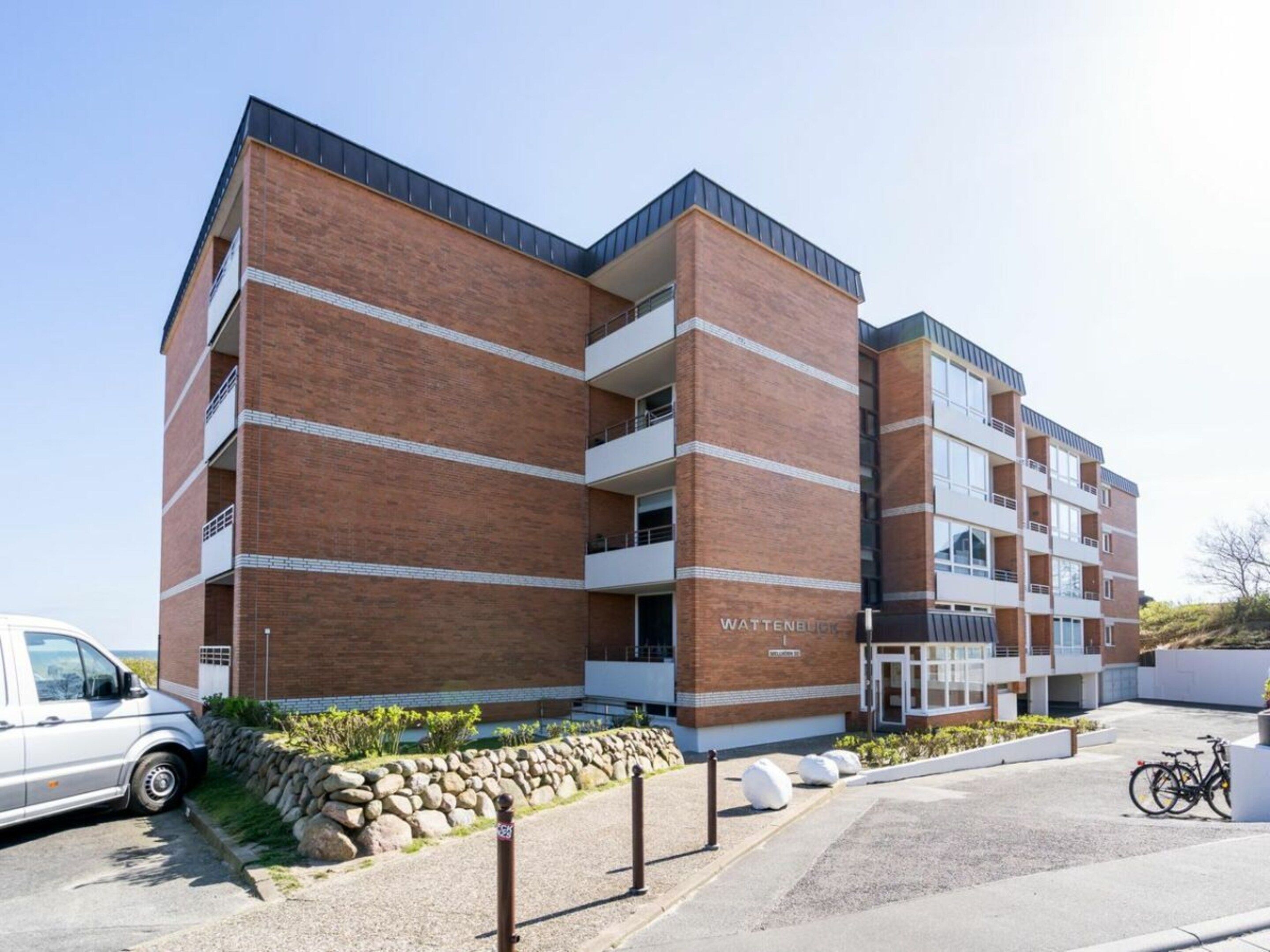 Un immeuble à plusieurs étages, doté d’une façade en briques, d’un toit plat et d’une enseigne sur laquelle on peut lire « WATTENBUCH ».