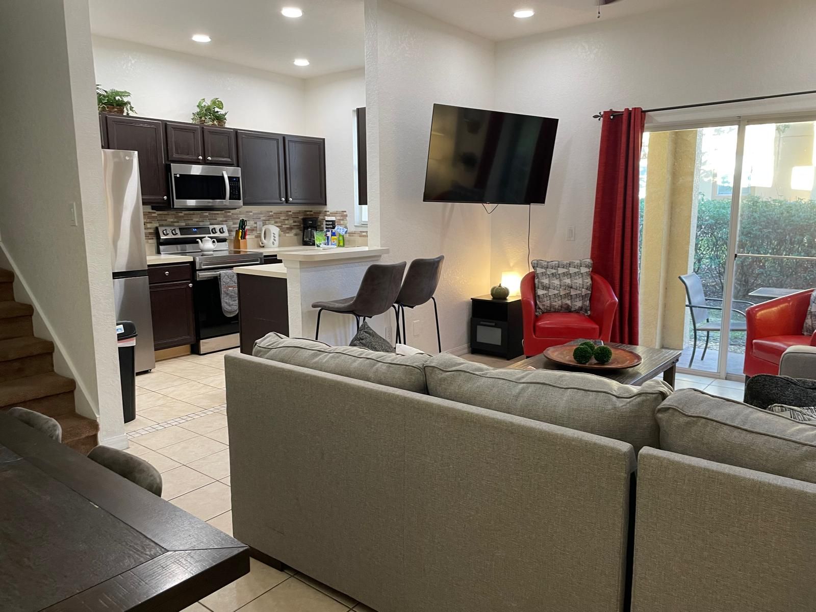 A modern living room with a sofa, a dining table, and a kitchen area with dark cabinets and a flat-screen TV.