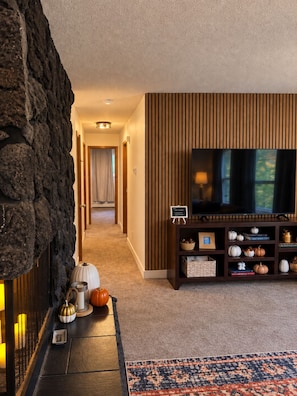 Een moderne woonkamer met een stenen openhaard, een flatscreen televisie op een houten standaard, en een decoratieve plank met pompoenen.