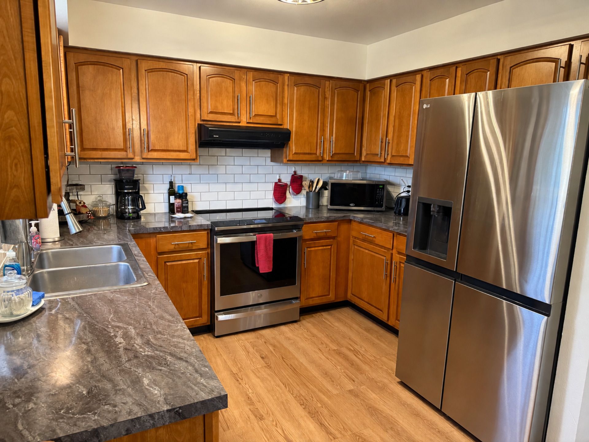 Una cocina con armarios de madera, electrodomésticos de acero inoxidable, encimera de mármol y salpicadero de azulejos.
