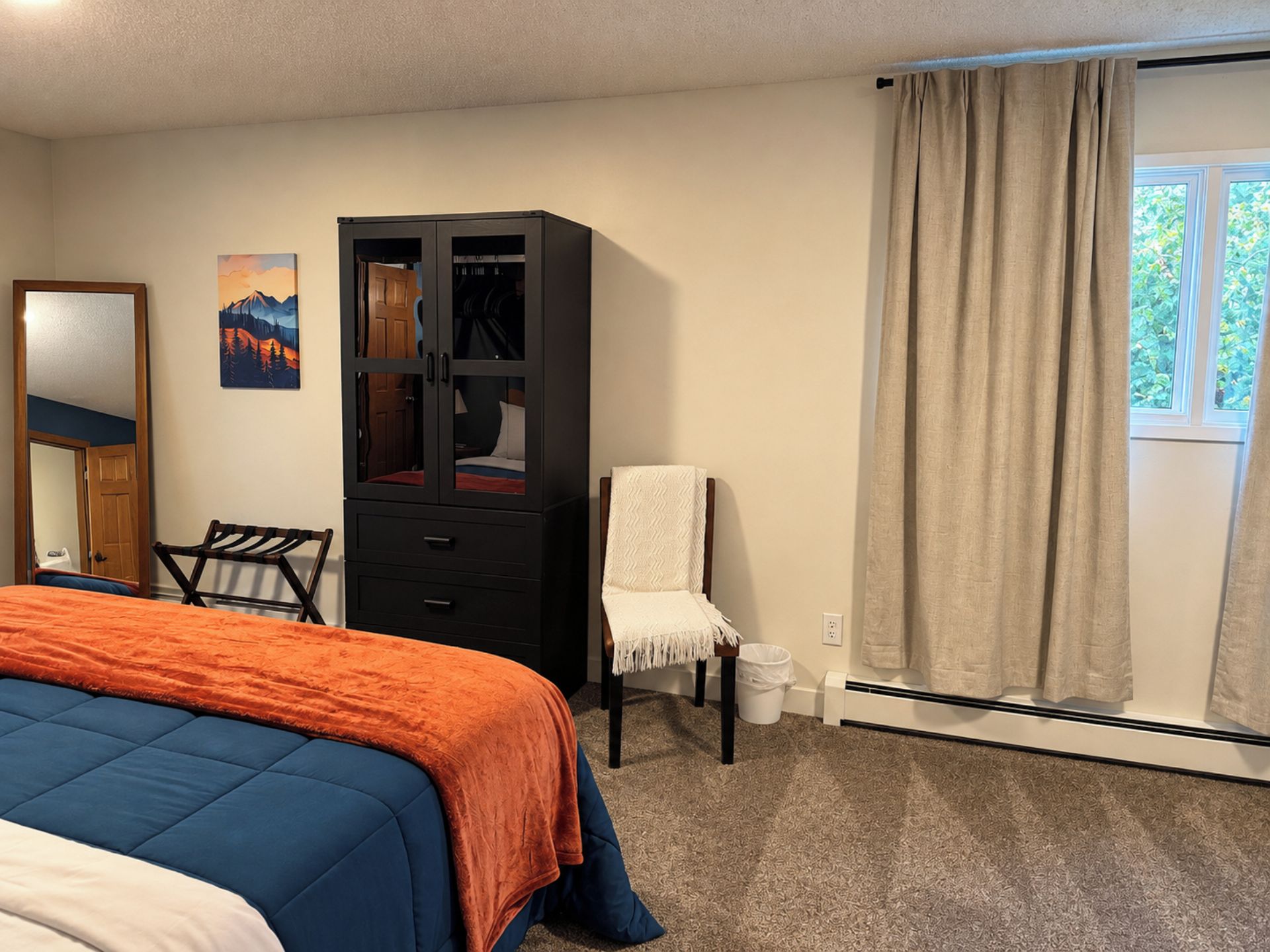 Une chambre à coucher avec un lit, une armoire, une chaise, une fenêtre avec des rideaux et un tableau accroché au mur.