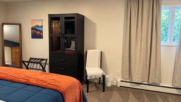 Une chambre à coucher avec un lit, une armoire, une chaise, une fenêtre avec des rideaux et un tableau accroché au mur.