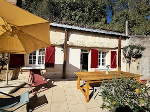 Een rustieke buitenruimte met een houten tafel en stoelen, een gele parasol en een stenen muur.