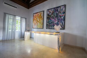 A modern interior with a marble reception desk, large abstract paintings, and a view of greenery through a window. - 15 Bedroom Villa in the Old City (Cartagena de Indias)