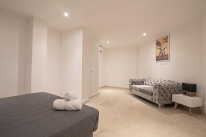 Un dormitorio con cama, un sofá gris, un televisor sobre un mueble de madera y un cartel en la pared.
