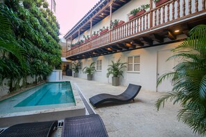 Un área de piscina con sillones de descanso, una piscina pequeña y un balcón con plantas en macetas.
