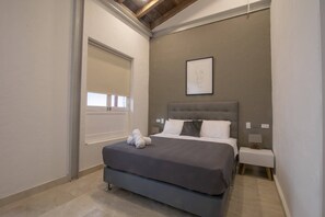 A bedroom with a double bed, a headboard, a bedside table, a nightstand, a framed picture on the wall, and a window with blinds. - 15 Bedroom Villa in the Old City (Cartagena de Indias)