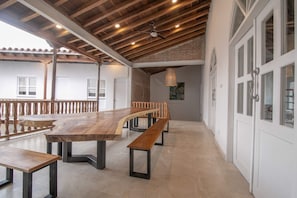 An indoor patio area with a long wooden table and benches, a ceiling fan, and a view of a brick building. - 15 Bedroom Villa in the Old City (Cartagena de Indias)