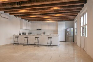 Una cocina moderna con armarios blancos, una isla central con taburetes de bar y un refrigerador de acero inoxidable.