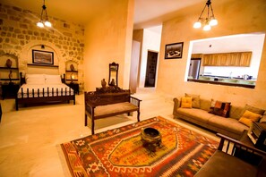 Una sala de estar acogedora con una pared de piedra, una cama, un sofá, un tapete estampado y una cocina visible a través de un arco.