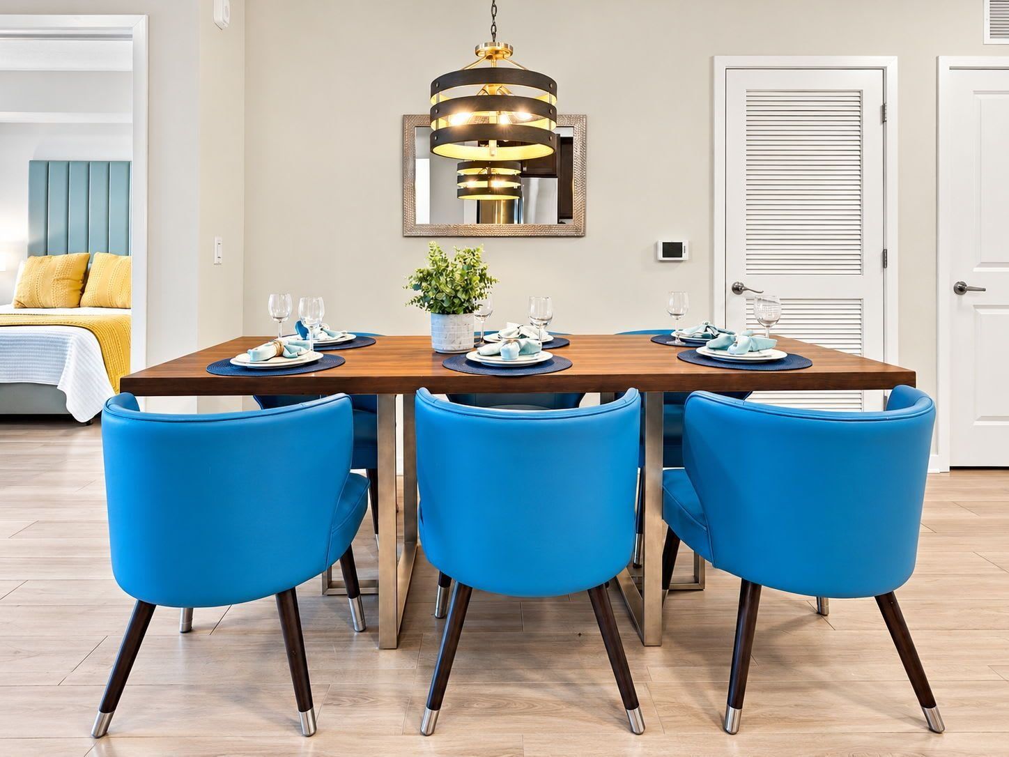 A dining area with a wooden table set for four, blue chairs, a hanging light fixture, and a potted plant.