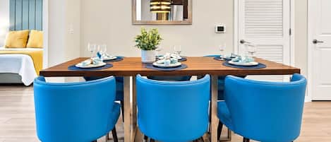 A dining area with a wooden table set for four, blue chairs, a hanging light fixture, and a potted plant.