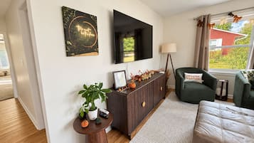 A modern living room with a dark wood console, a flat-screen TV, a green armchair, and a view of the outdoors.