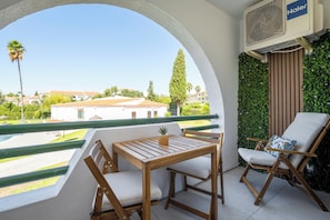 A balcony with a wooden table and chairs, a potted plant, and a view of buildings and trees. - Fado Apartment | Pool, Balcony & Near the Beach – Albufeira (Albufeira)