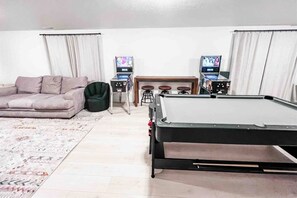 Un salon comprenant une table de billard, un canapé, un fauteuil en forme de poire, deux tabourets de bar et deux téléviseurs.