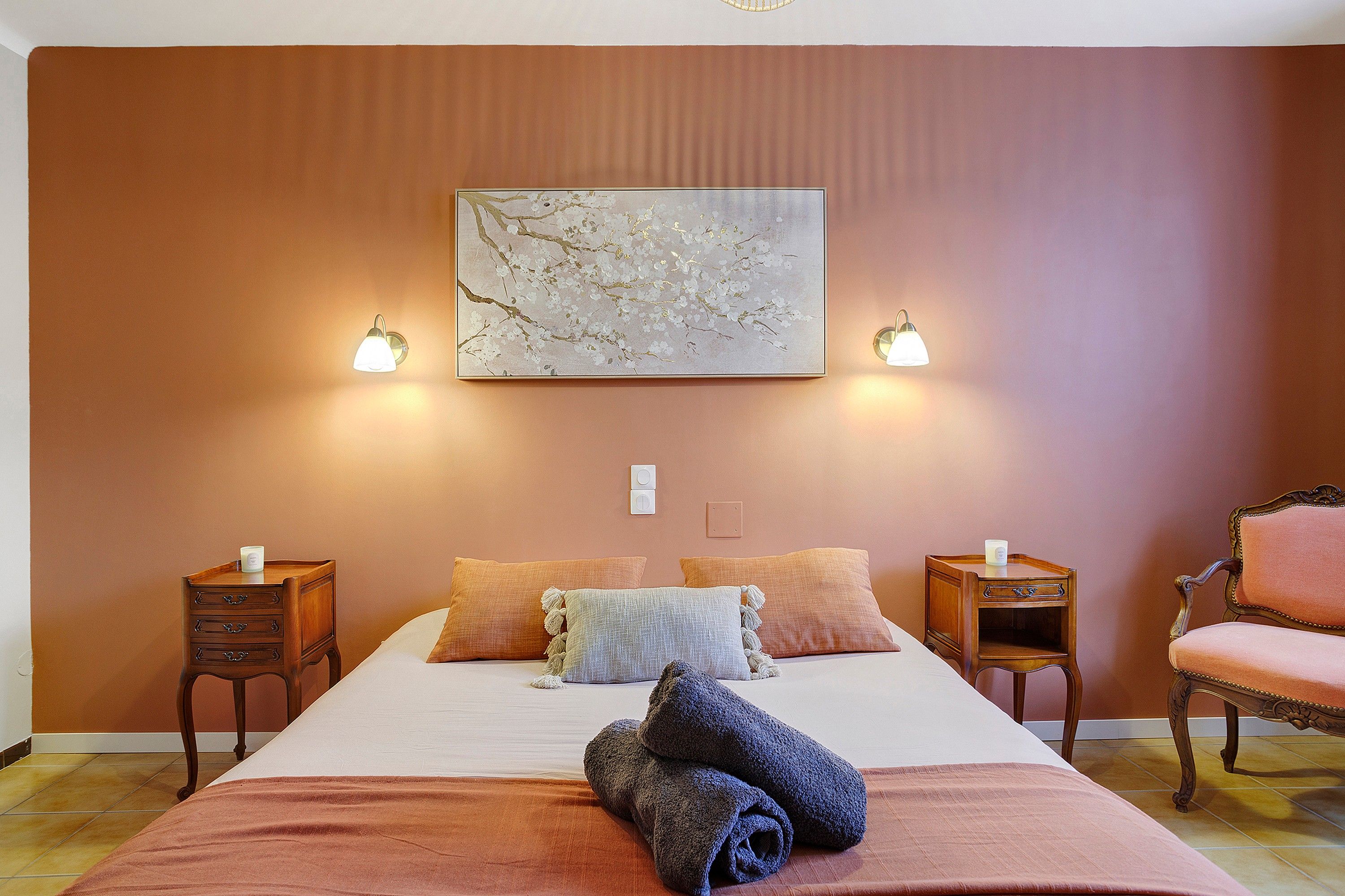 Ein Hotelzimmer mit einem großen Bett, zwei Nachttischen, einem Sessel und einem an der Wand hängenden Kunstwerk.