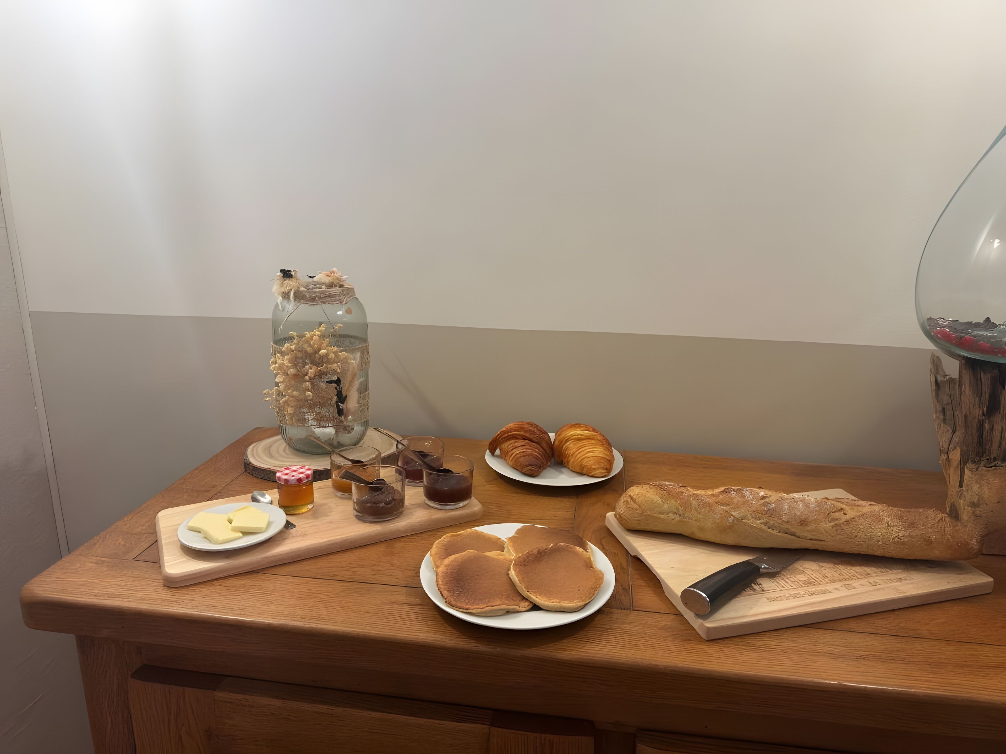 Et træbord med mad, blandt andet kager, brød og pandekager, samt et dekorativt glas.