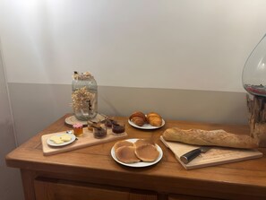 Une table en bois sur laquelle sont disposés divers aliments, notamment des pâtisseries, du pain et des crêpes, ainsi qu'un bocal en verre décoratif.