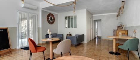 A spacious living area with a round wooden table, two chairs, a sofa, and a television.
