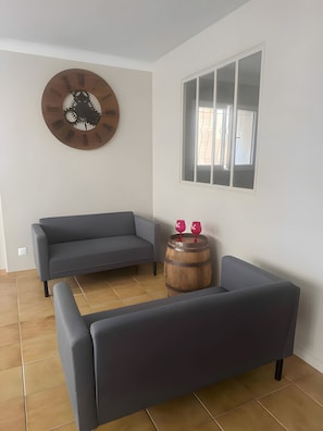 Una sala moderna con un sofá gris, un barril de madera y un reloj de pared original.