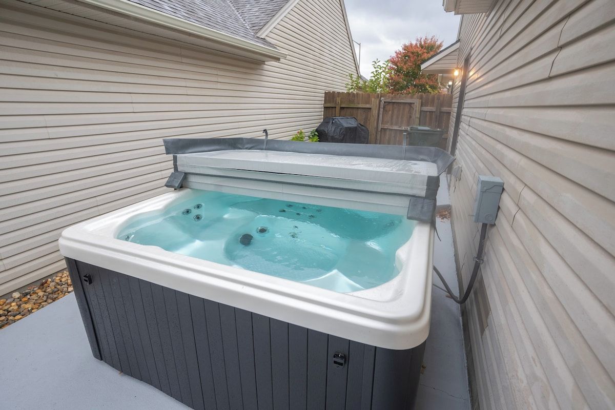 A hot tub in a backyard with a wooden fence and a house in the background.