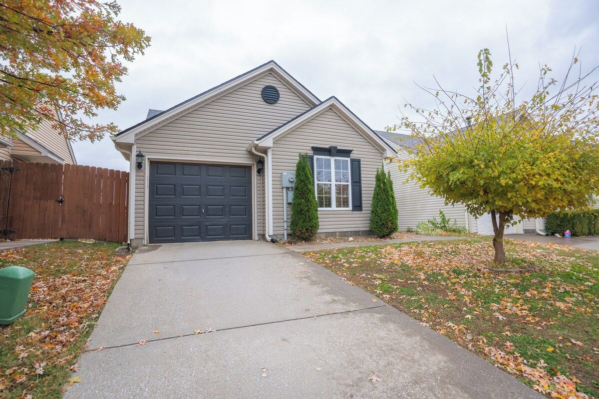 A single-story house with a garage, a front yard with a tree, and a wooden fence.