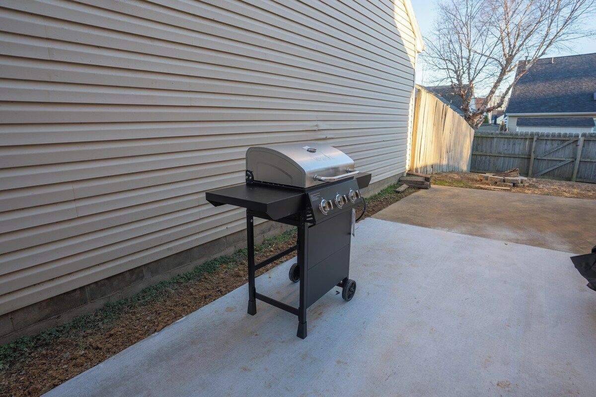 A portable barbecue grill with a digital display, positioned on a concrete patio next to a house with horizontal siding.