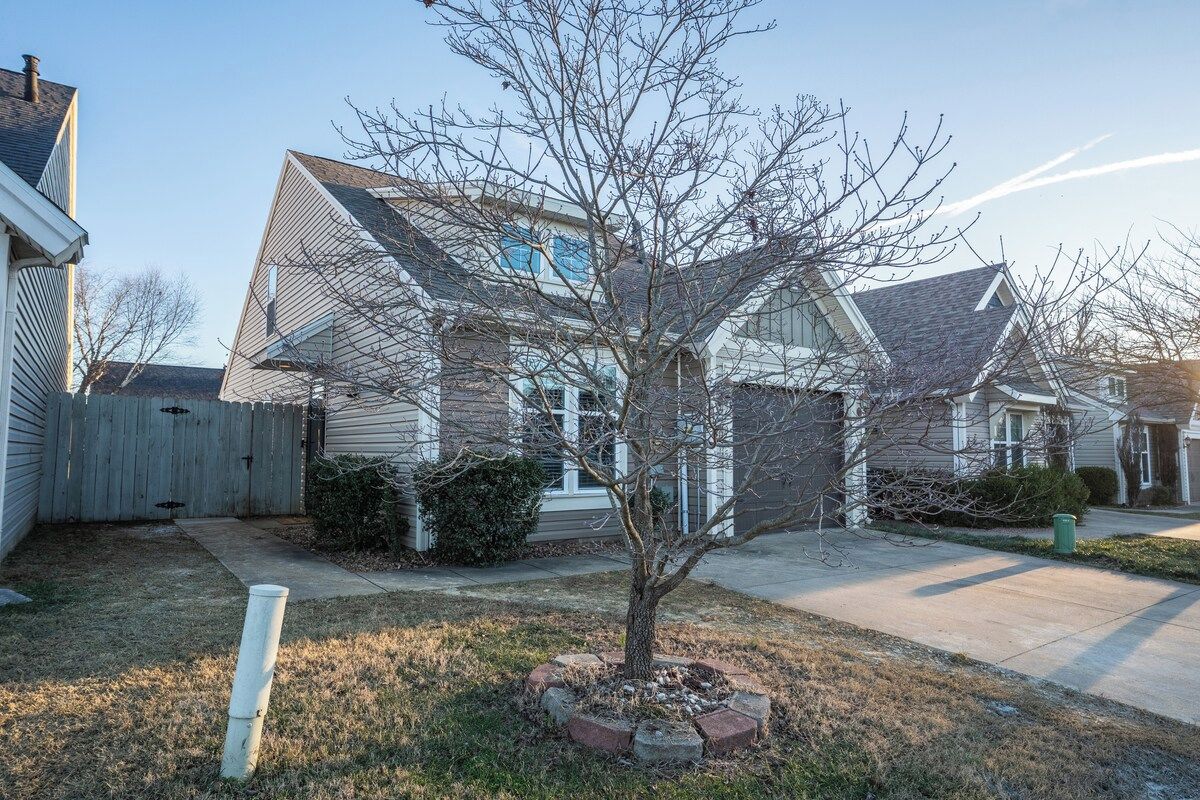 A residential house with a front yard, a wooden fence, and a tree.