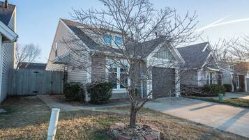 A residential house with a front yard, a wooden fence, and a tree.