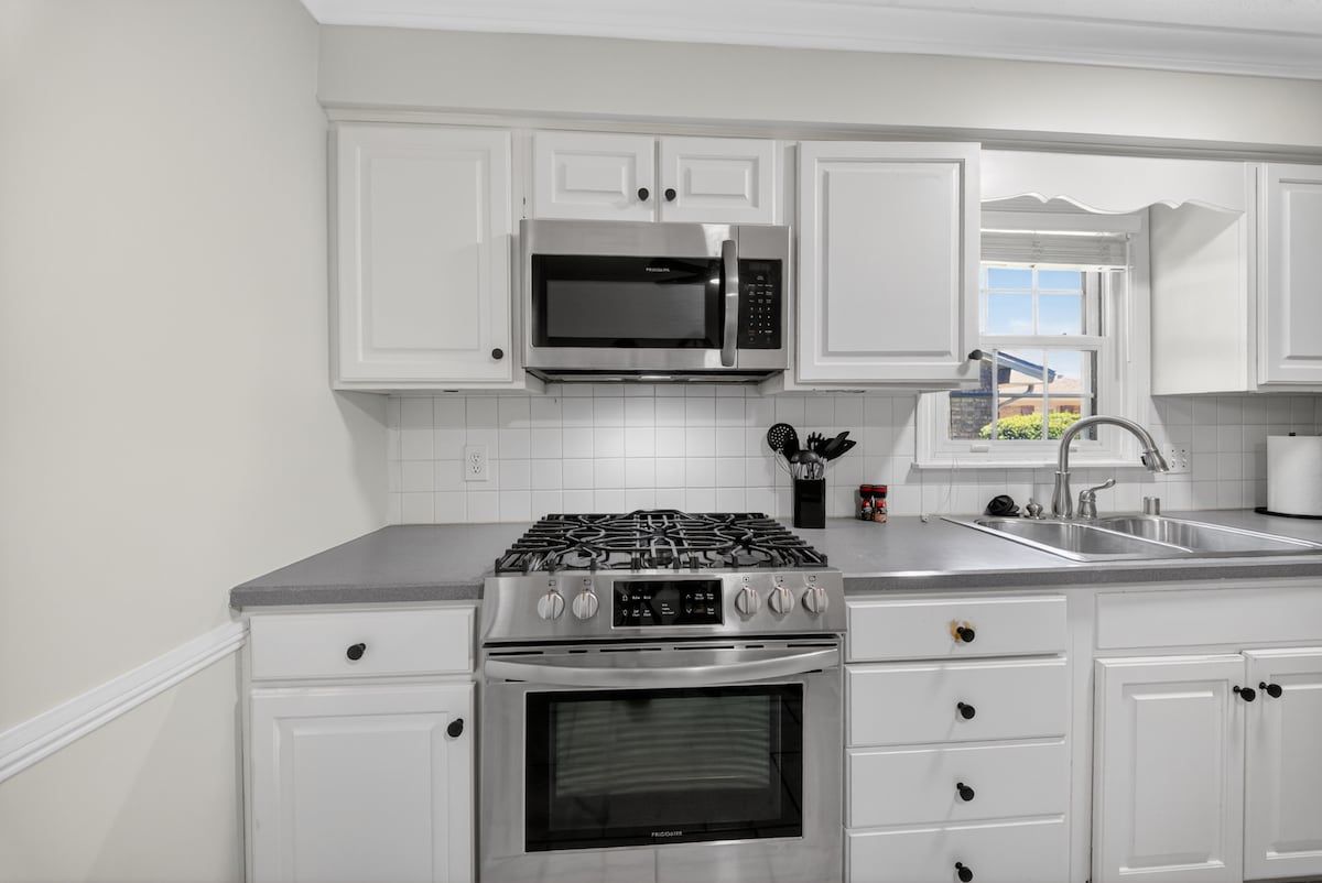 A modern kitchen with white cabinetry, stainless steel appliances, and a window providing a view.