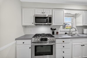 A modern kitchen with white cabinetry, stainless steel appliances, and a window providing a view. - Bluegrass Springdale | Air Hockey & Darts (Owensboro)