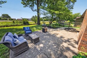 An outdoor patio area with a wicker sofa, a wooden table, and a grill. - Bluegrass Springdale | Air Hockey & Darts (Owensboro)