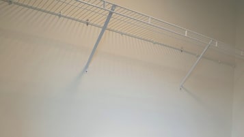 A room with a metal wire shelf holding folded white bedding.
