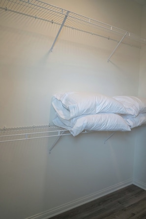 A room with a metal wire shelf holding folded white bedding. - Bluegrass Nest- Sleeps 8 (Owensboro)
