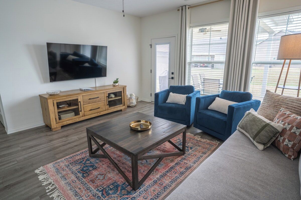 Un salon avec un téléviseur, un meuble en bois, un canapé bleu et un tapis à motifs.