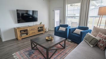 Un salon avec un téléviseur, un meuble en bois, un canapé bleu et un tapis à motifs.