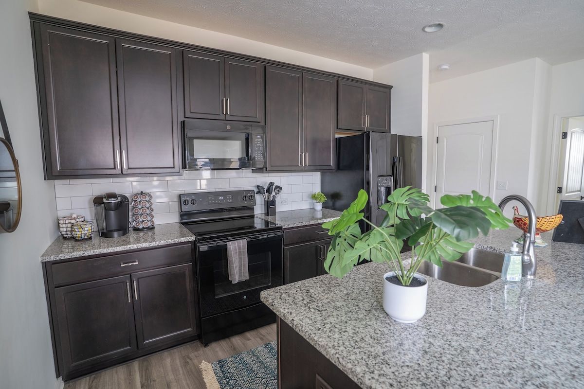A modern kitchen with dark cabinetry, stainless steel appliances, and a granite countertop.