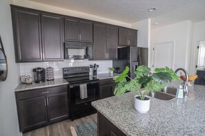 A modern kitchen with dark cabinetry, stainless steel appliances, and a granite countertop. - Bluegrass Nest- Sleeps 8 (Owensboro)
